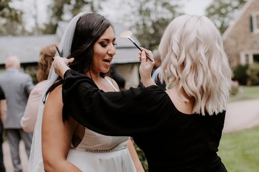 Makeup artist applying final touches to a bride's makeup outdoors during wedding preparations