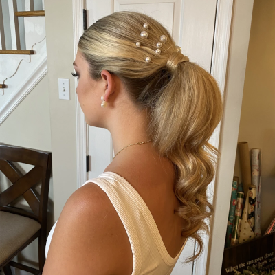 Elegant high ponytail with cascading curls and scattered pearl pins, showcasing modern bridal hair with classic details
